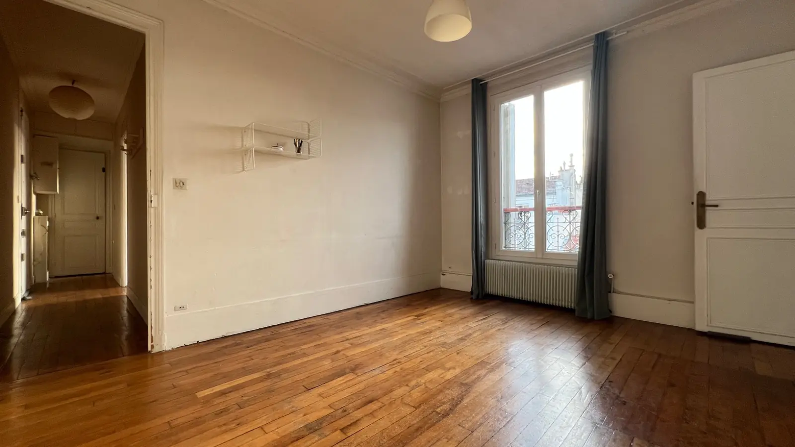 Pièce lumineuse avec parquet, fenêtre sur les toits et accès au couloir