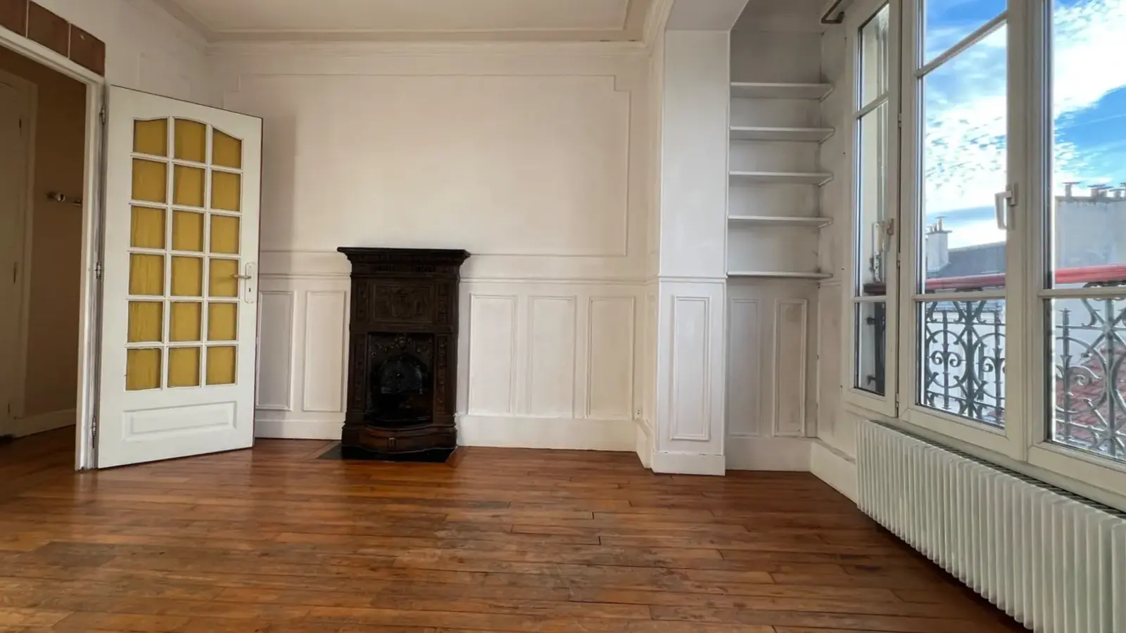 Salon lumineux avec parquet, poêle prussien et vue dégagée sur les toits de Paris