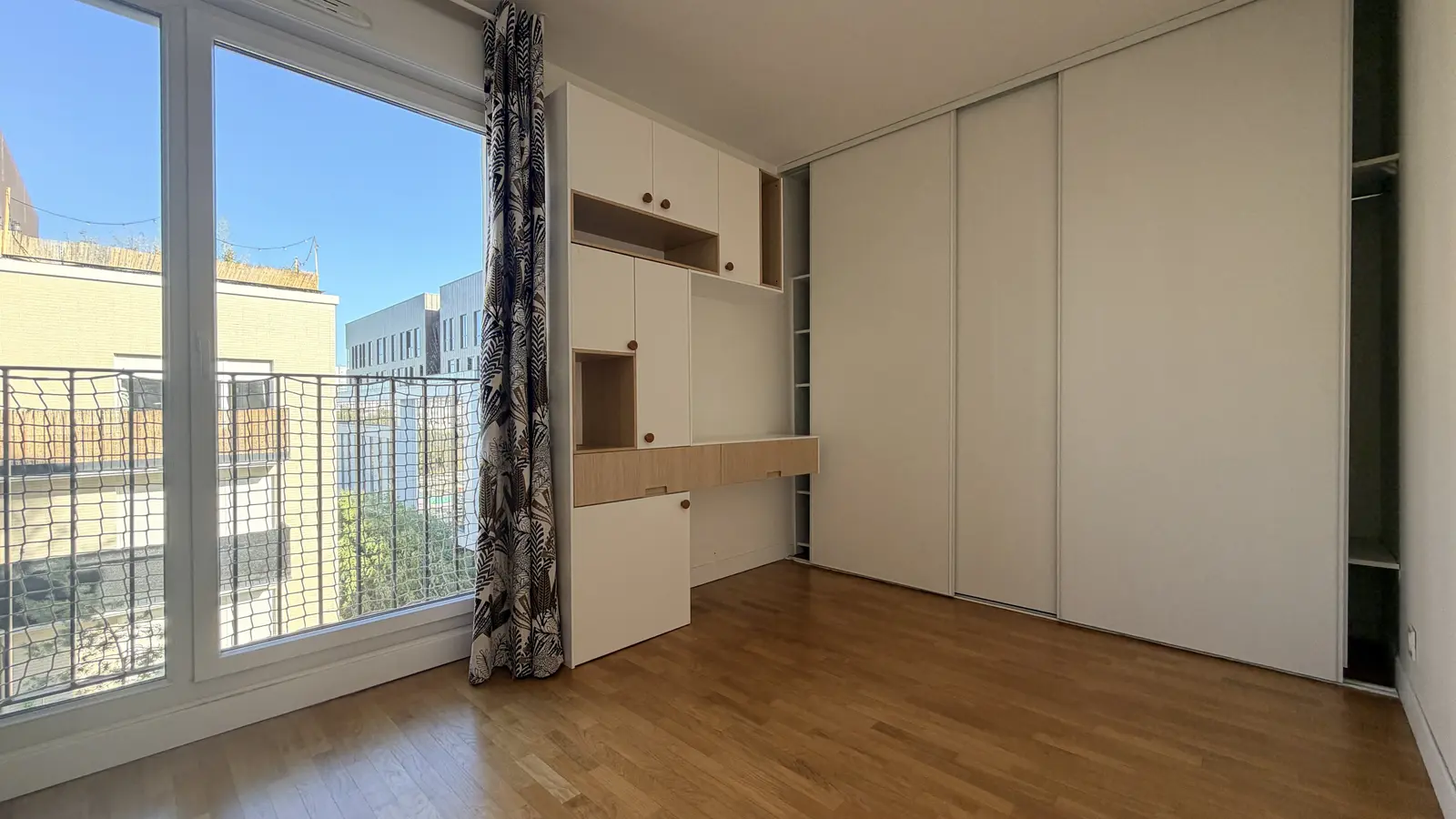 Chambre vide avec parquet, rangements intégrés et porte-fenêtre