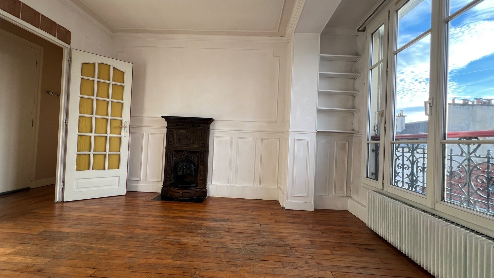 Salon lumineux avec parquet, poêle prussien et vue dégagée sur les toits de Paris