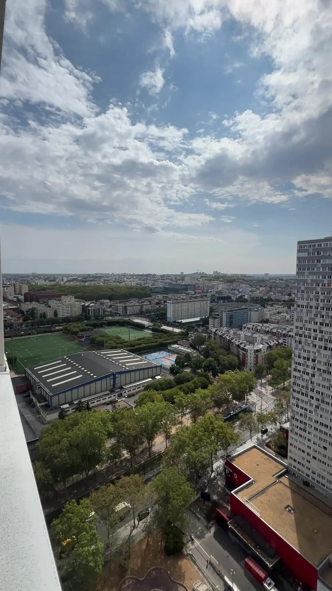 Vue latérale dégagée au-dessus du boulevard et des terrains de sport, immeuble voisin à droite